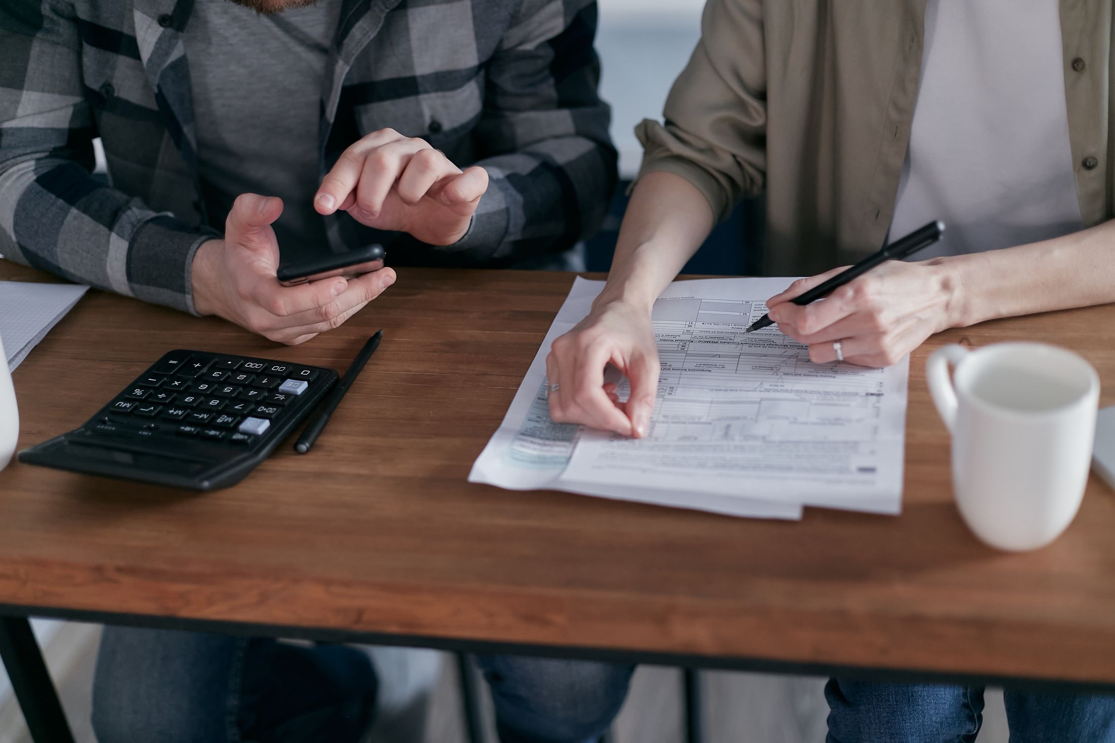 Two people at a table reviewing tax documents with a calculator and a pen